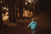 a toddler in a coat walking on a path in a forest 
