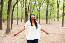 woman with open arms standing outdoor in a forest 