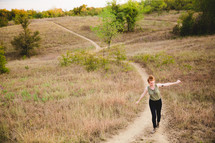 woman walking on a path up a hill with open arms 
