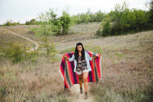 Woman walking up a hill wrapped in a blanket 