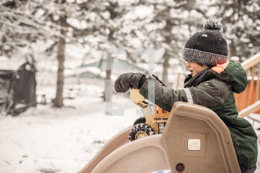 boy playing with a toy truck outdoors in the snow 