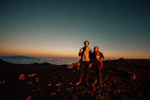 a couple holding hands standing on a mountaintop at sunrise 