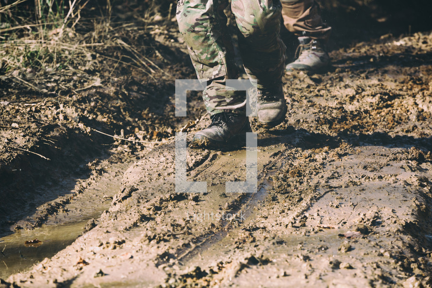 Brown military boots on mud and puddle