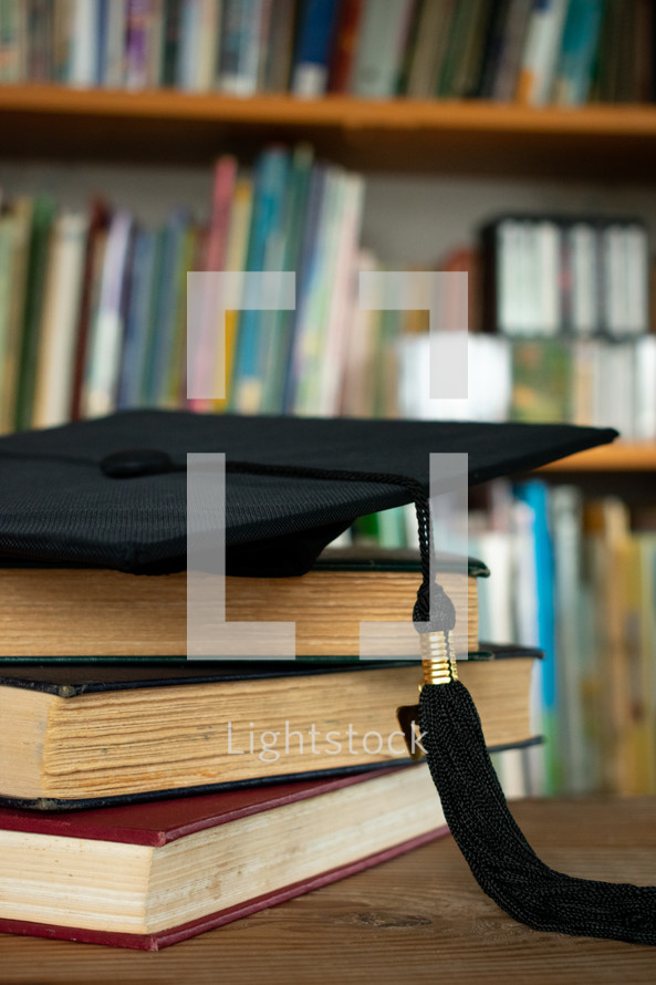 graduation cap on a stack of books on a desk in a library 