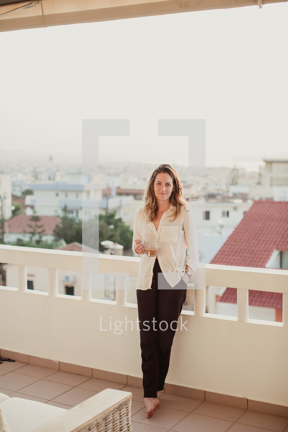 A woman standing on a balcony with a cup of coffee.