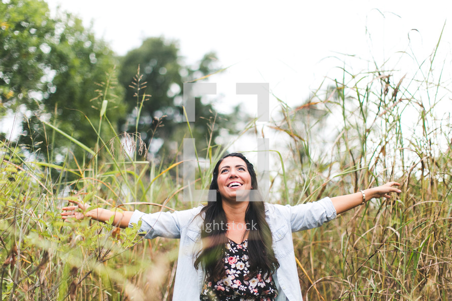 woman with open arms standing outdoors in tall grass 