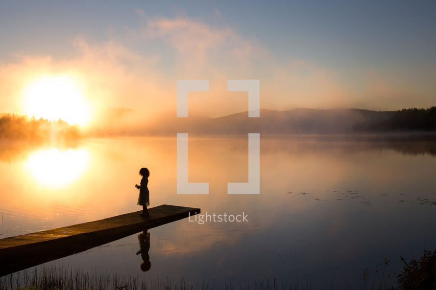 a girl on a pier over a steaming lake at sunrise 