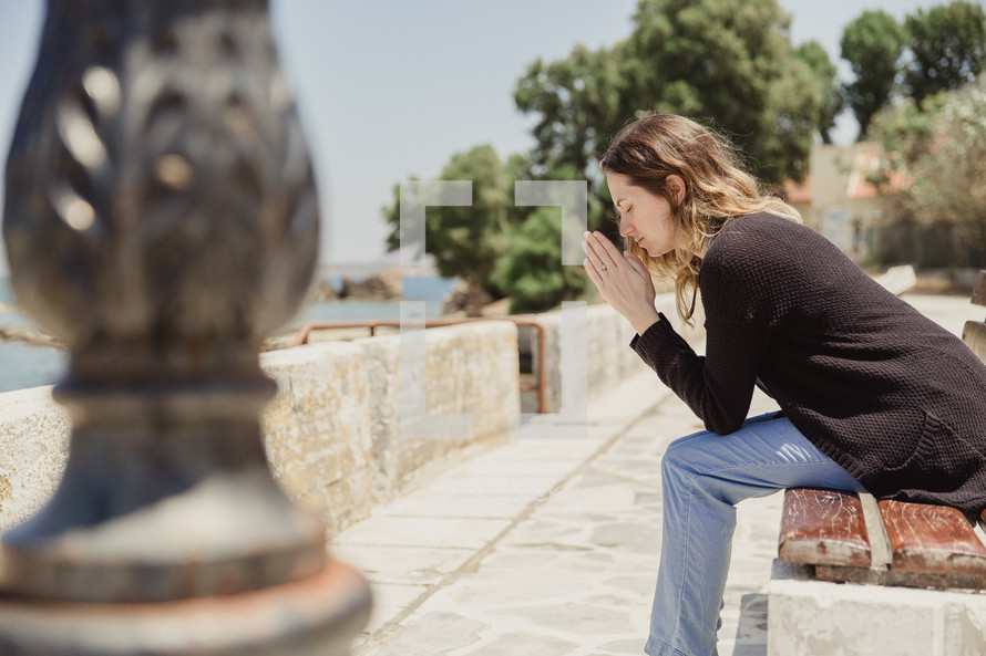 woman saying a prayer sitting on a bench in Greece 