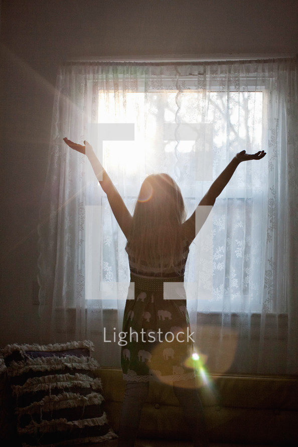 woman standing in front of a window with raised arms 