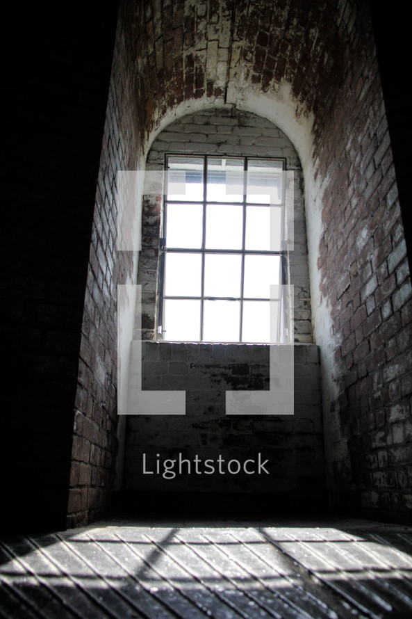 A narrow arched brick room with  a window through which the sun is shining.