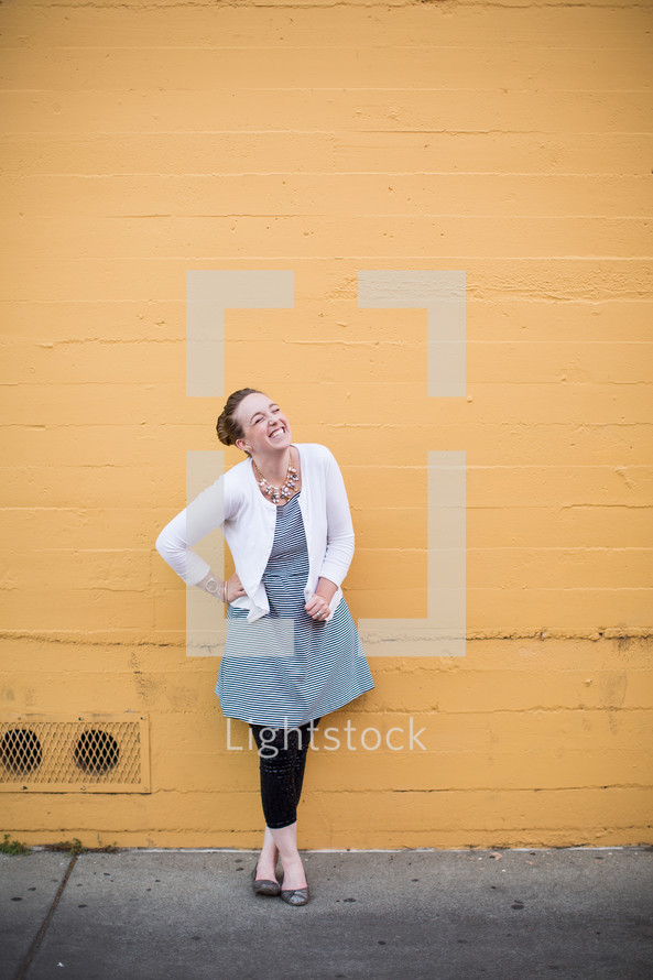 a smiling woman in a dress standing in front of a yellow wall 
