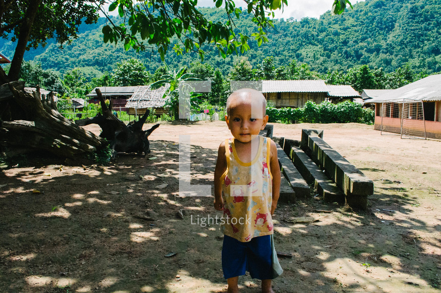 a toddler boy standing barefoot in the dirt 