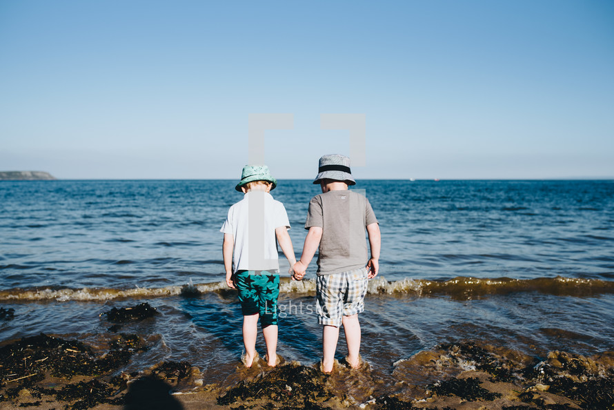 brothers holding hands standing on a rocky beach 