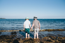 brothers holding hands standing on a rocky beach 