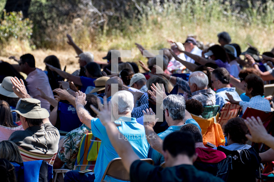 an outdoor prayer service, people with hands raised 