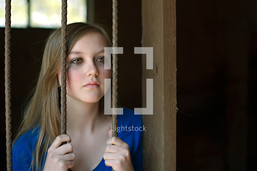 teen girl hiding behind bars with tears in her eyes 