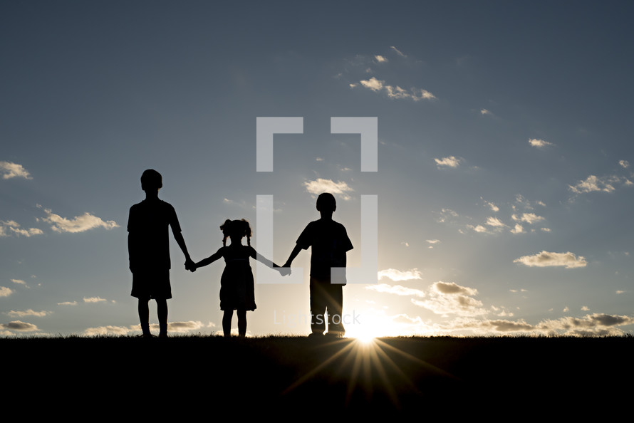 silhouettes of children holding hands outdoors 