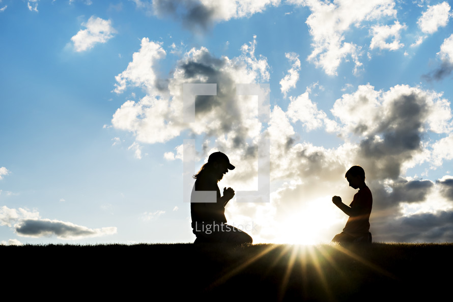 silhouette of a mother and child kneeling in prayer between a sunburst 