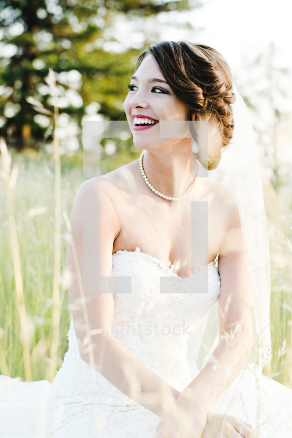 a smiling bride sitting in tall grass