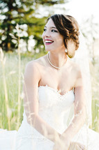 a smiling bride sitting in tall grass