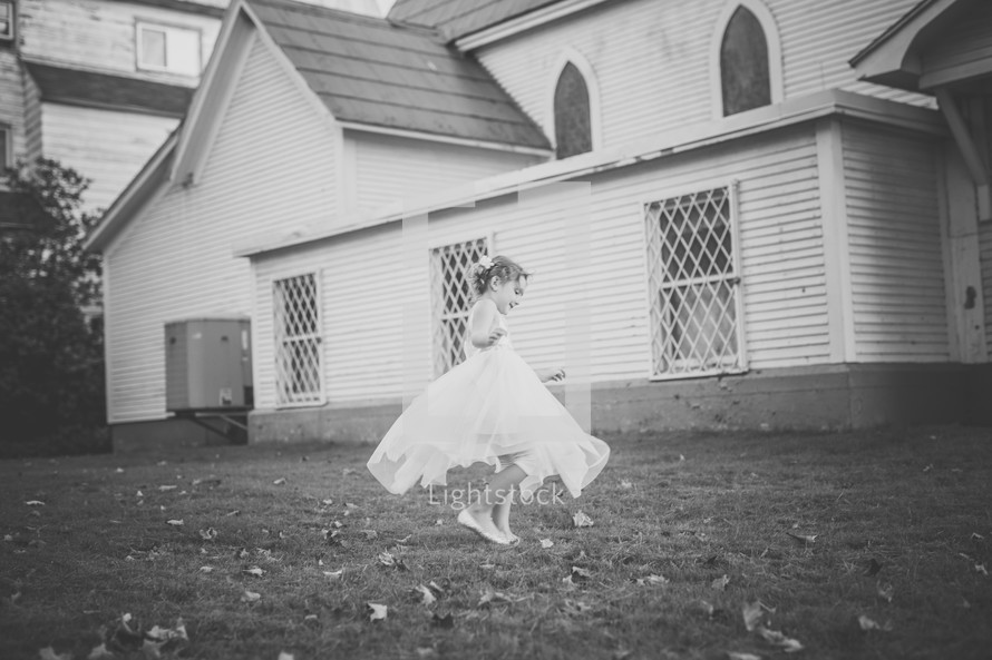 a girl in a dress playing in fall leaves in front of a church 