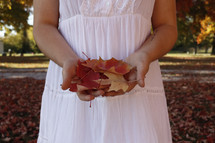 a woman in a white dress holding fall leaves 
