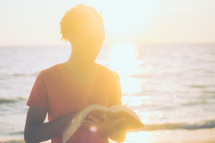 man standing on a beach reading a Bible