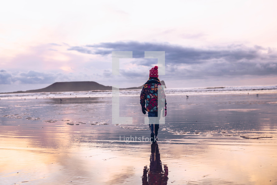 a girl walking on a wet sand on a beach in winter 
