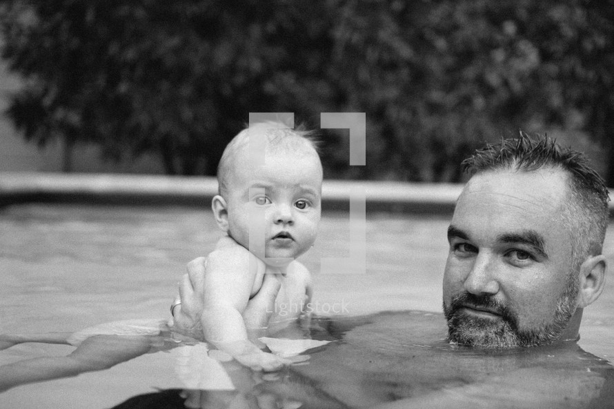 father and infant son swimming in a pool 