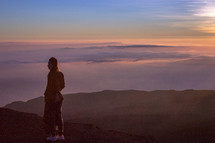 a woman standing on a mountaintop above the clouds looking out 