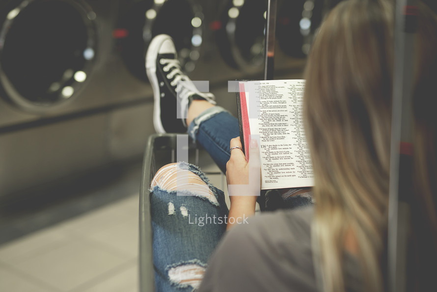 a woman reading a Bible at a laundry mat 