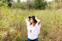 woman in a black hat standing in tall grasses 