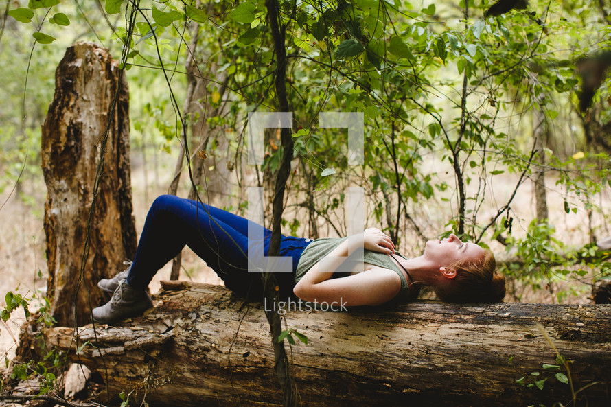 woman lying on a fallen tree in a forest 