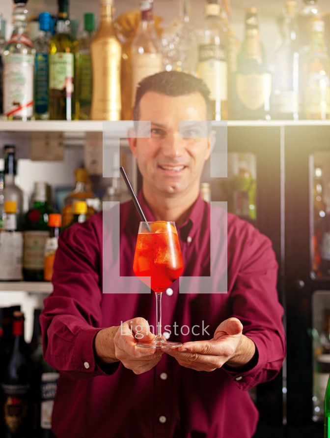Smiling male bartender offering a freshly made cocktail in a modern bar setting
