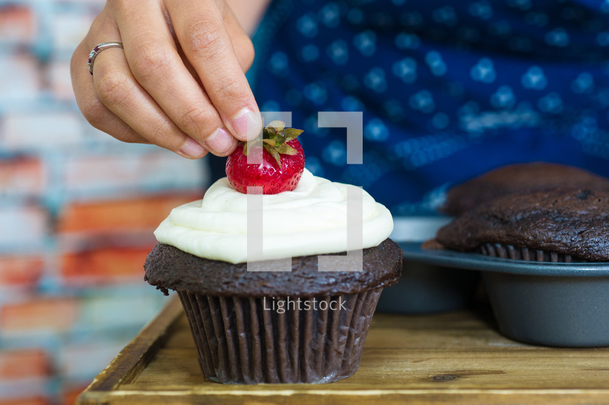 woman adding a strawberry to a chocolate cupcake 