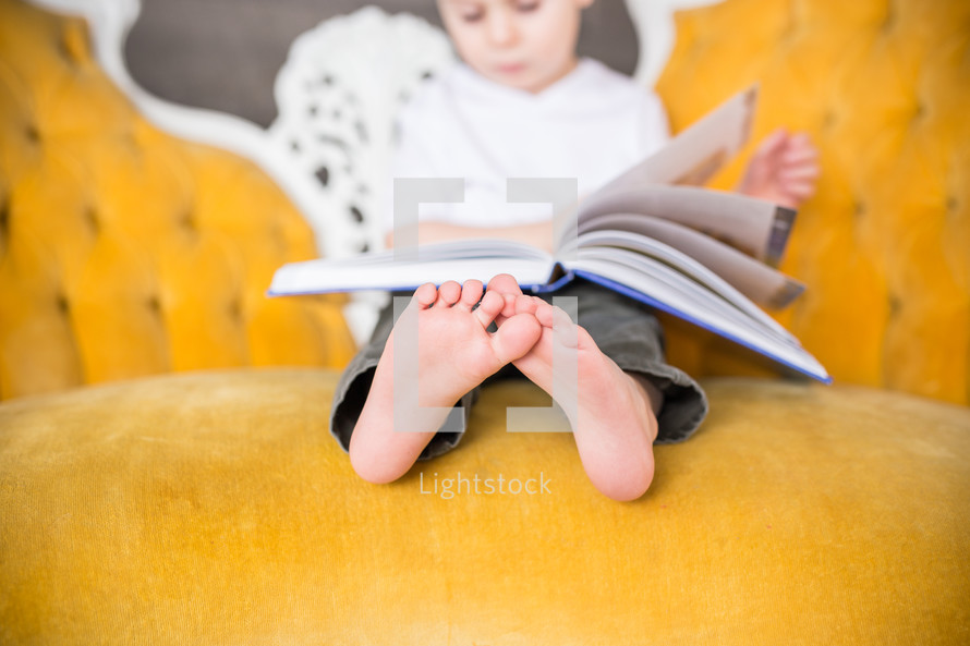 a boy child sitting on a couch reading a book 