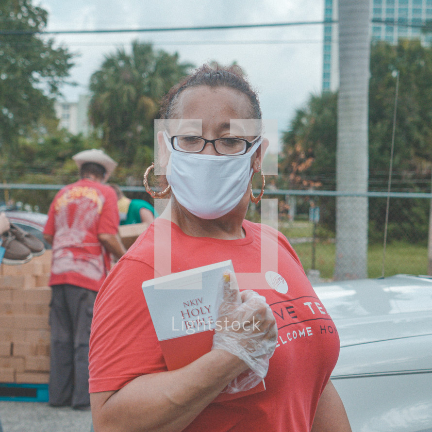a woman wearing a face mask handing out Bibles 