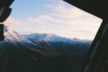 View of a snow covered mountain range from a plane window.