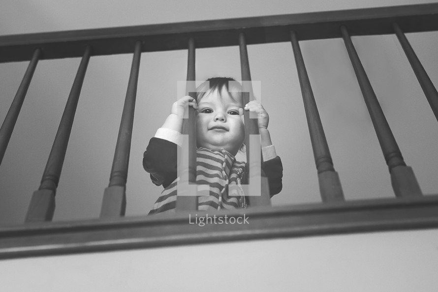 toddler looking through stair railings 