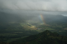 rainbow peeking through the clouds over a green landscape 