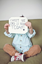toddler holding a sign that reads Christ the Lord has risen today!