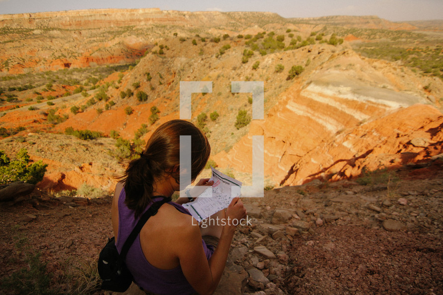 a woman sitting outdoors at the top of a canyon at sunset looking at a map