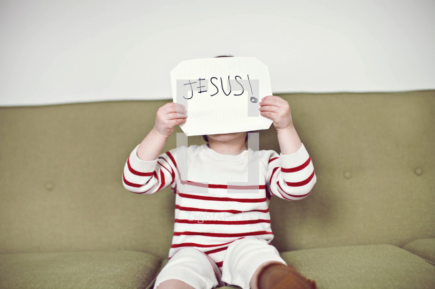child holding up a sign with the word Jesus on it 
