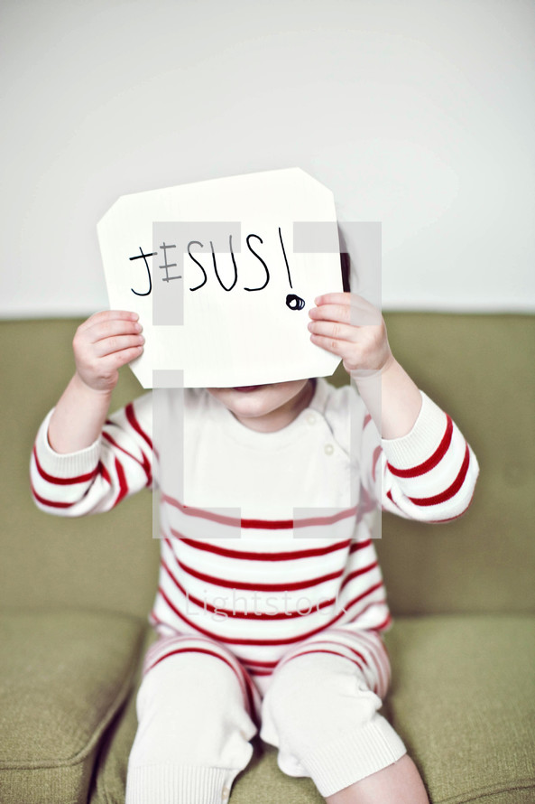 child holding up a sign with the word Jesus on it 