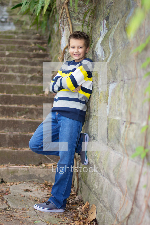 Young boy standing and posing against a old stone wall