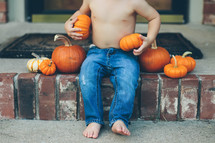 toddler boy sitting on steps with pumpkins 
