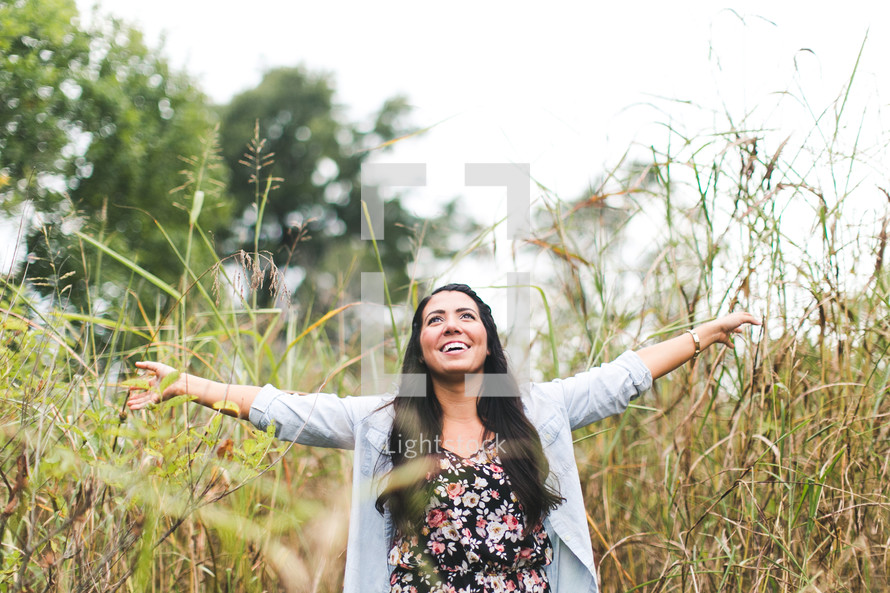 woman standing outdoors in tall grass with open arms 