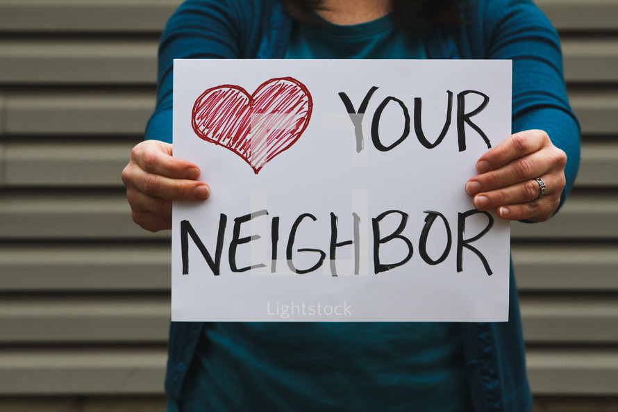 A woman holding a sign that reads love your neighbor.