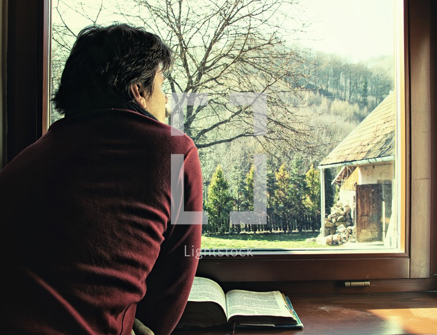 a man reading a Bible and looking out a window 