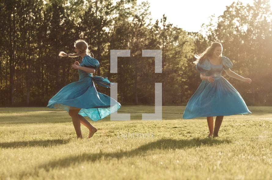 Two young women in blue dresses dancing in a field.